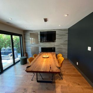 Modern dining room with a long wooden table, mustard chairs, black accent wall, and sliding glass doors