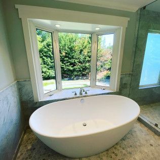 Freestanding oval bathtub in a bright bathroom with large windows and green garden view