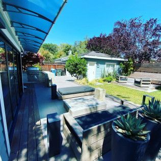 Modern backyard patio with seating, awning, shed, and purple-leaf trees