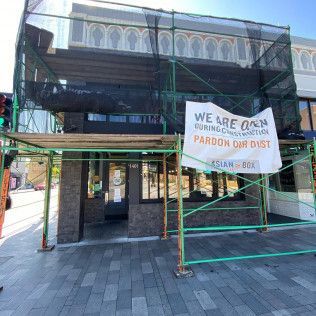 Covered storefront with green scaffolding and a sign reading “We Are Open” for a barber district.