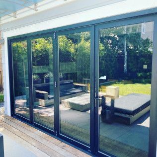 Modern glass patio doors opening to an outdoor lounge with white cushions and green lawn