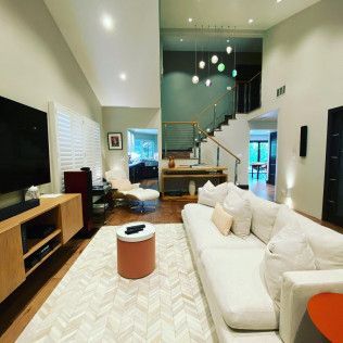 Modern living room with white sofa, rug, TV, and staircase under pendant lights