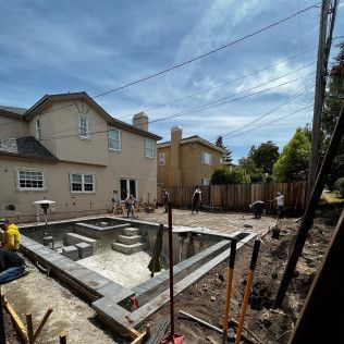 Backyard pool under construction beside beige houses, with exposed concrete and building materials.