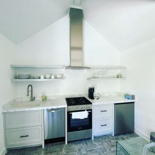 Modern white kitchen with stainless appliances, open shelves, and a skylight under a sloped ceiling