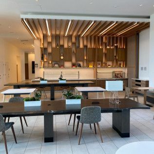 Modern lobby lounge with long tables, gray chairs, white tile floors, and a warm wood feature wall.