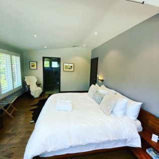Bright bedroom with white bedding, gray accent wall, wood floor, and a door to an adjoining room.