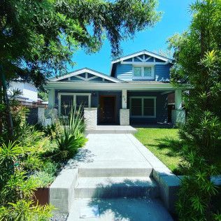 Modern house with a front porch, concrete walkway, and lush green landscaping under a blue sky