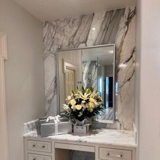 Elegant white vanity with marble backsplash, mirror, gift boxes, and a flower arrangement in a bright hallway.