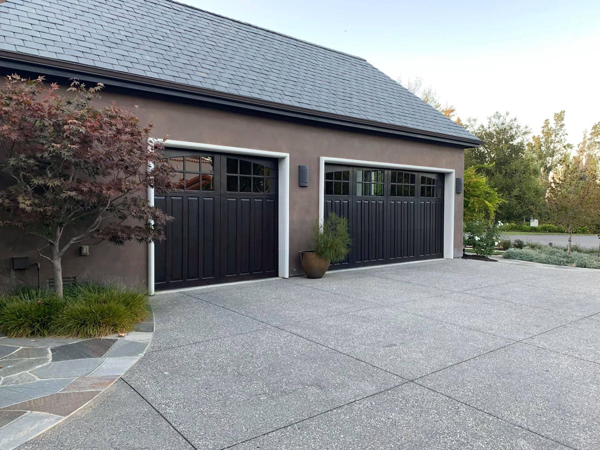 Modern house exterior with two black garage doors and a large gravel driveway