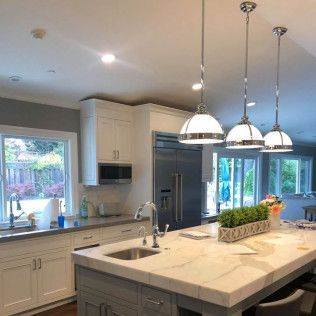 Modern kitchen with white cabinets, large island, pendant lights, and a stainless-steel refrigerator.
