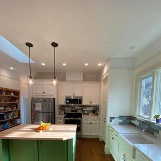 Bright modern kitchen with white cabinets, island, pendant lights, and large windows.