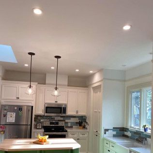 Bright white kitchen with island, pendant lights, stainless appliances, and a window over the sink.