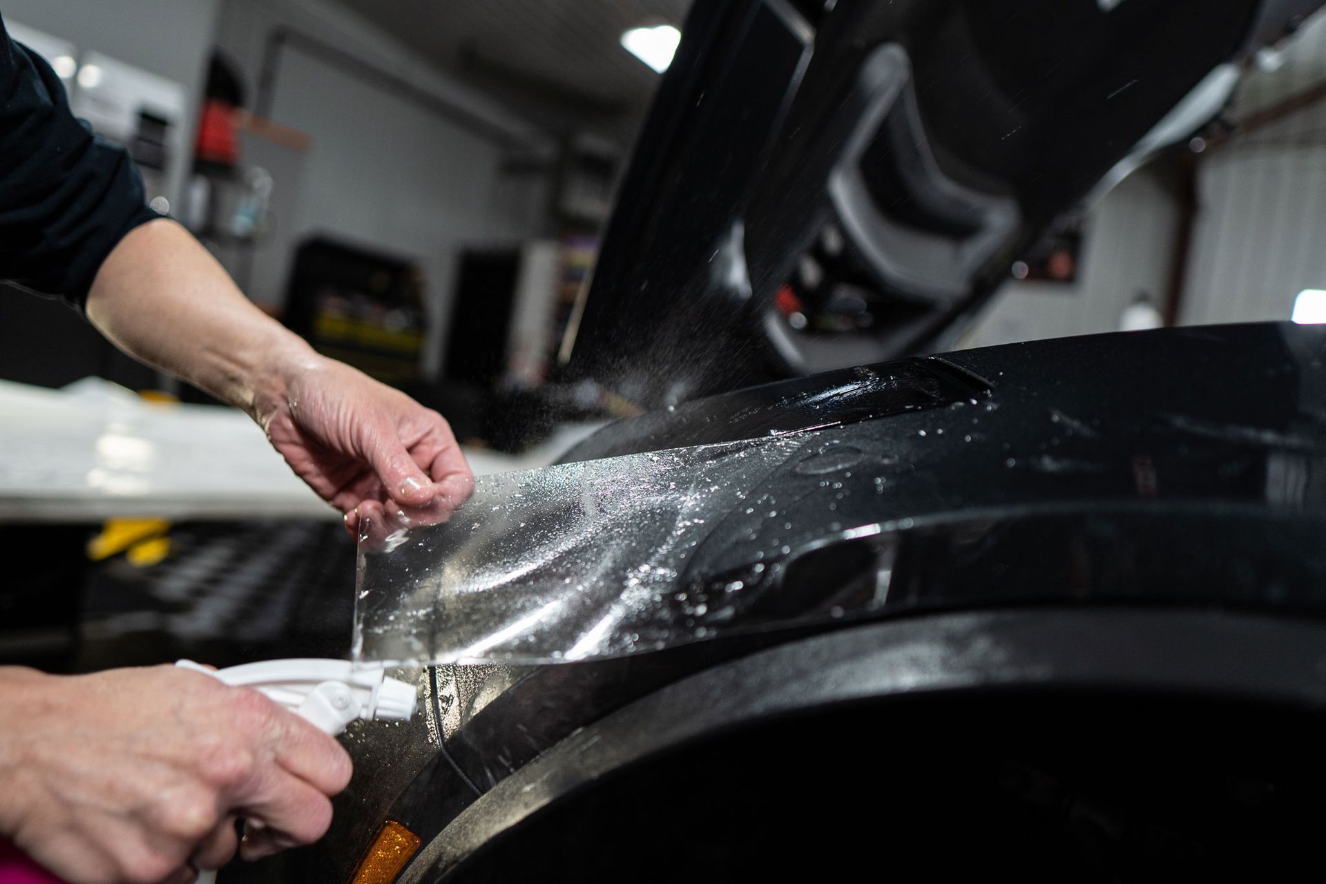 A person is applying protective film to the fender of a car.