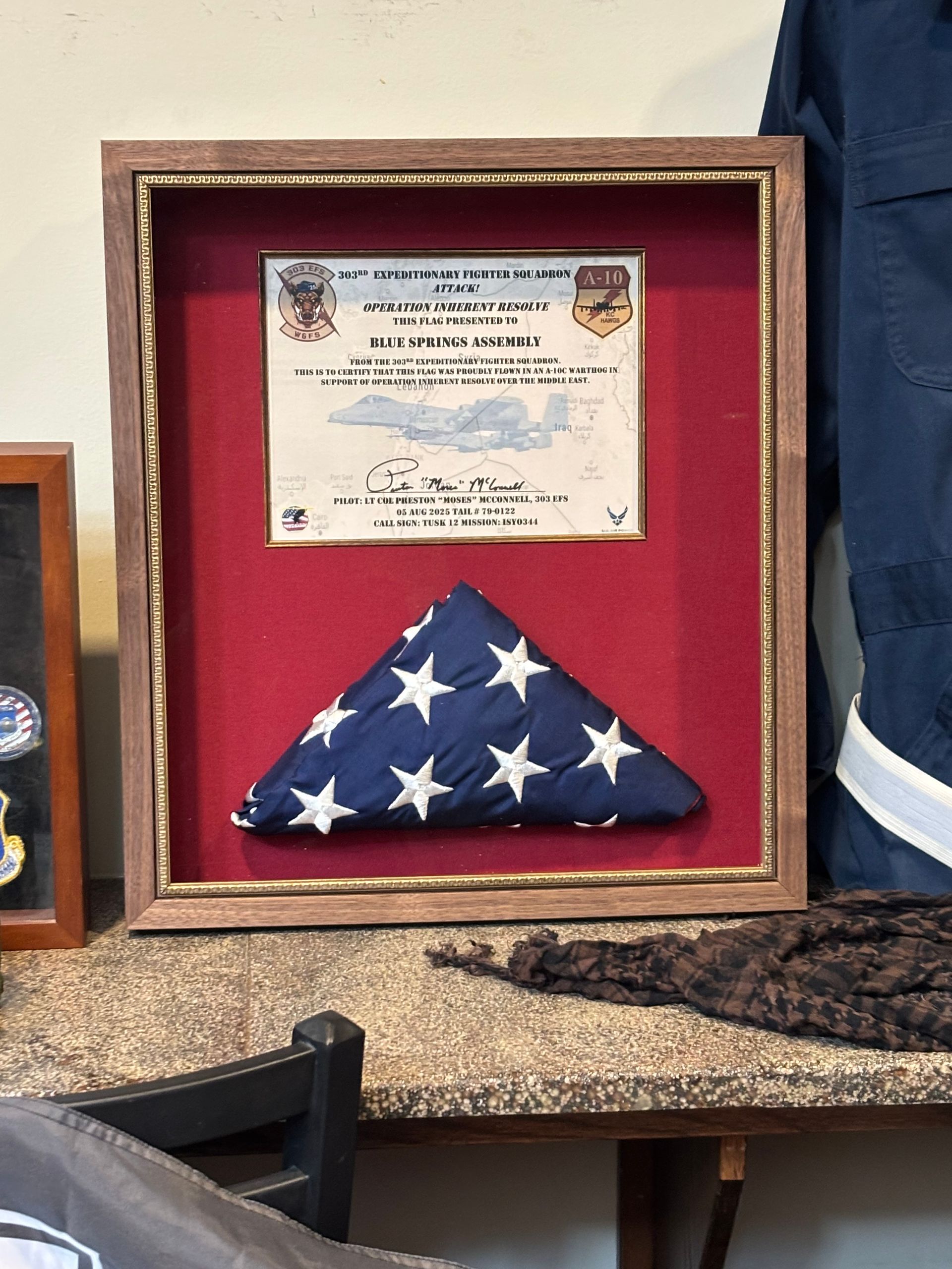 A shadow box displays a folded American flag and a certificate of appreciation from the U.S. Air Force on a red background.