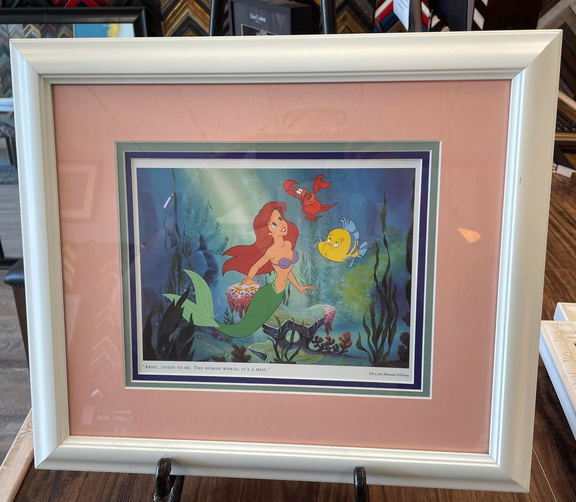 A framed print of Ariel, Flounder, and Sebastian from The Little Mermaid against an underwater background.