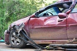 A broken down car sits on the side of the road with broken windows.