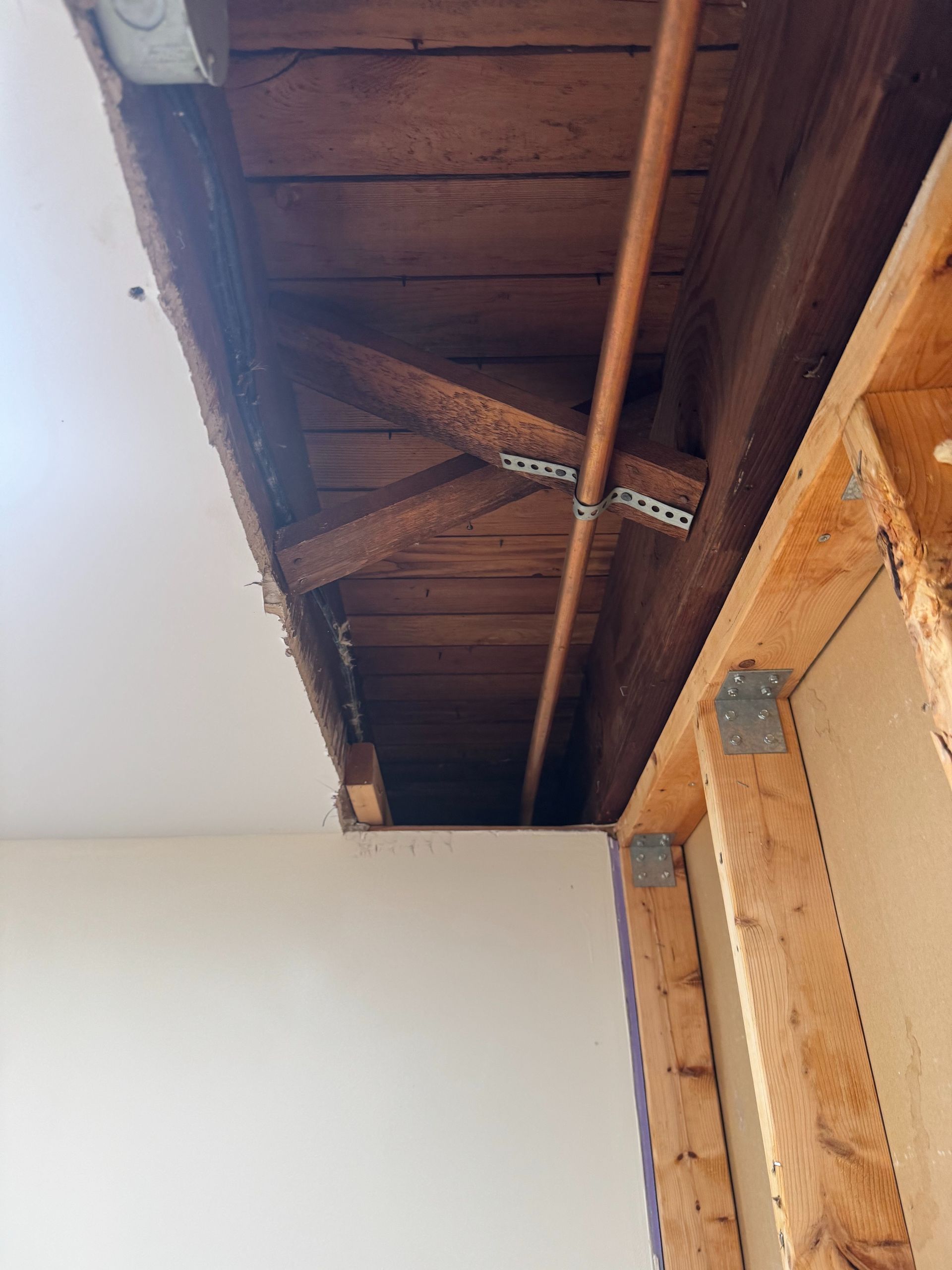 Damaged ceiling with exposed wooden beams and a broken section above an interior wall.