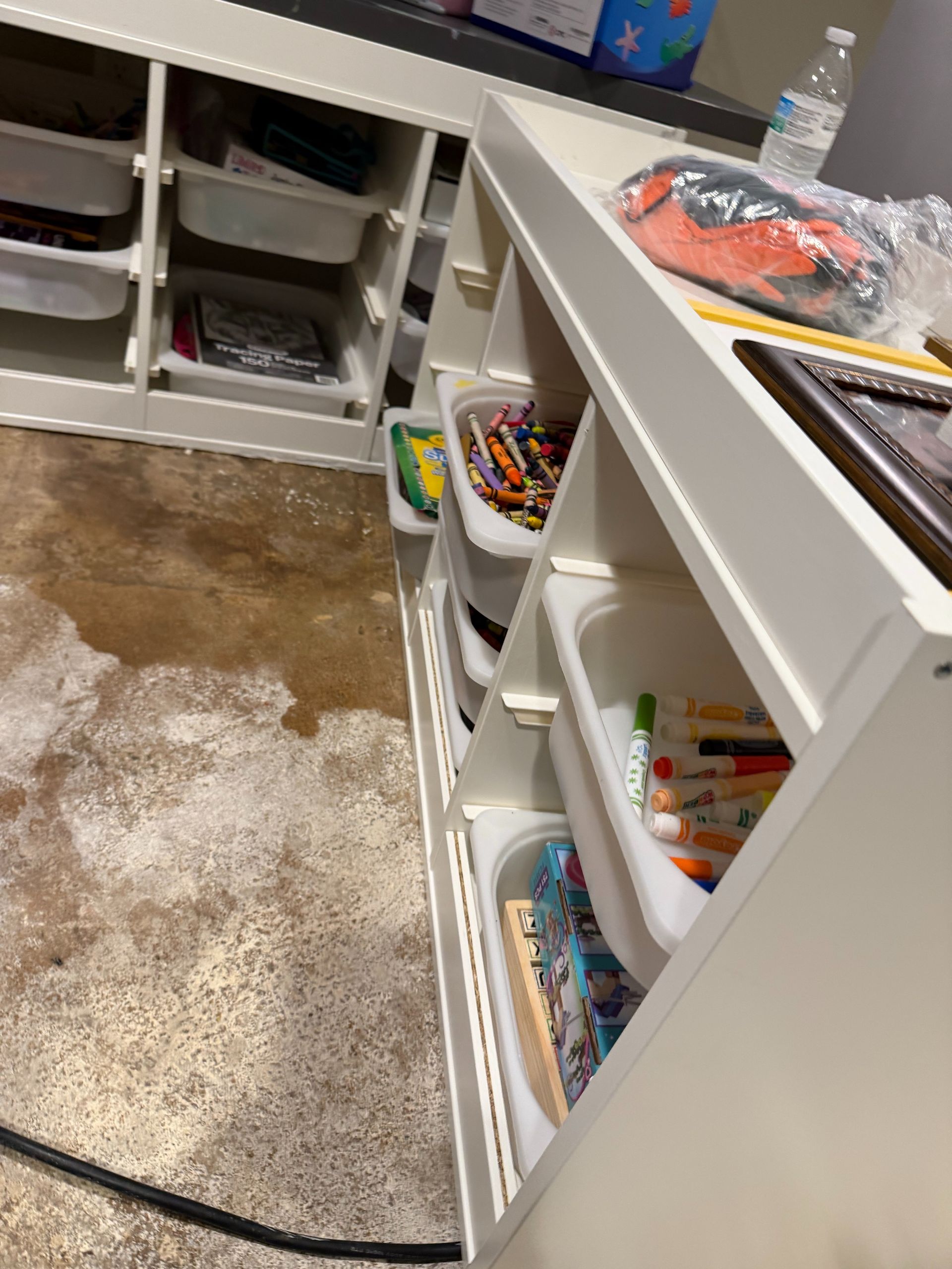 Open drawers with art supplies and crayons in a craft room, with a carpeted floor and countertop.