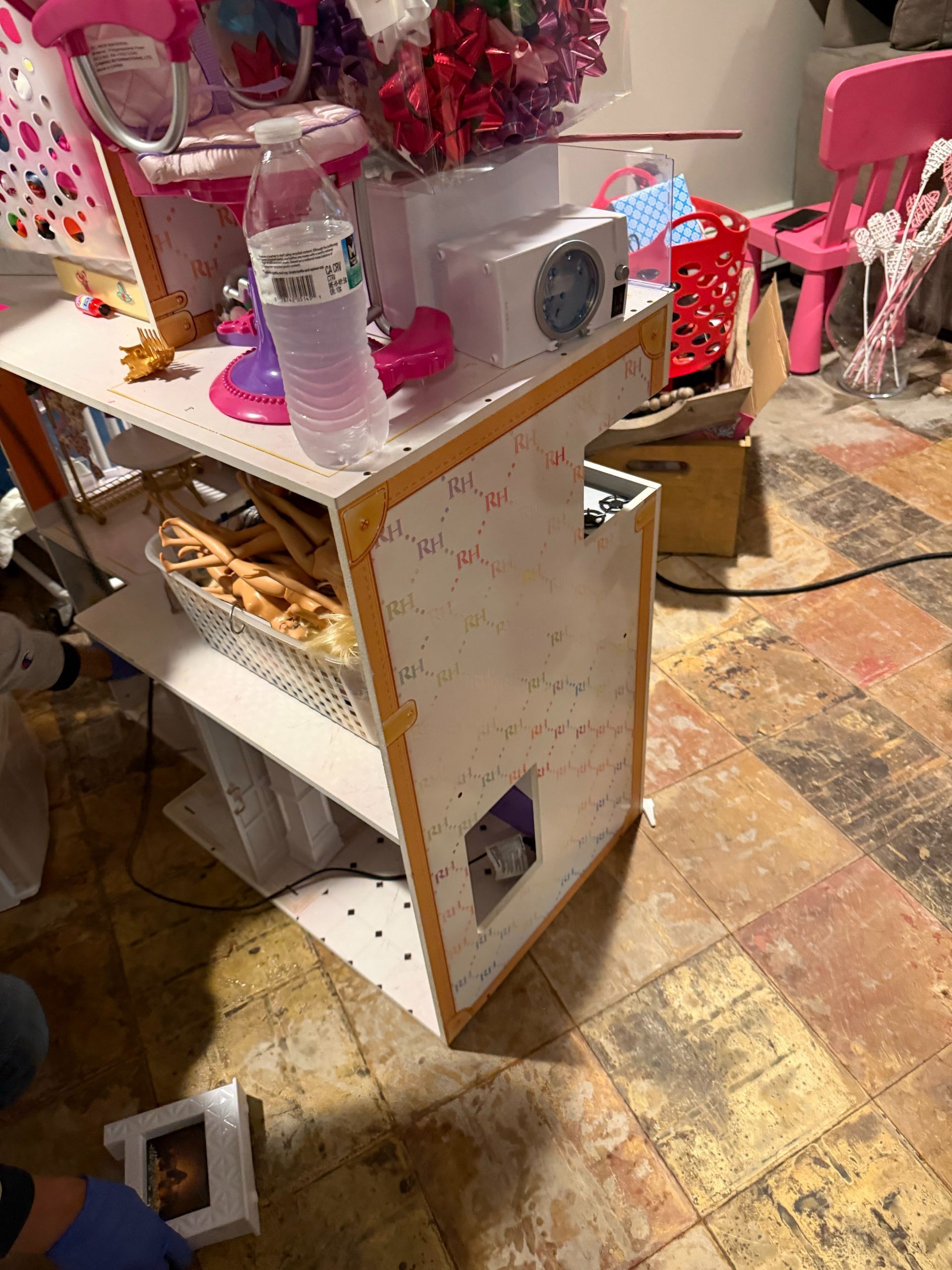 Pink-decorated shelf with a radio, water bottle, and mirror on a cluttered floor