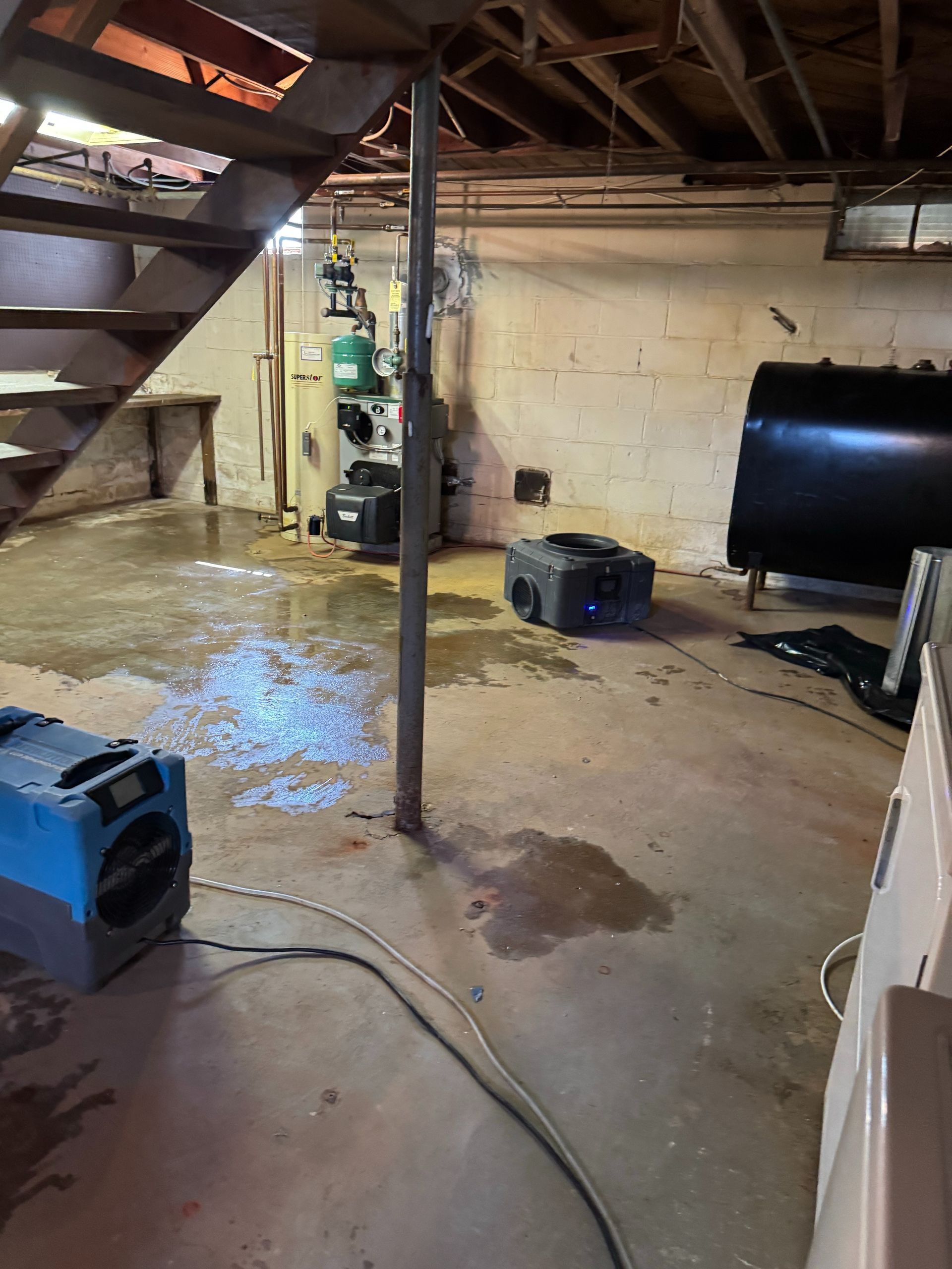 Flooded basement with wet concrete floor, stairs, a support pole, and utility equipment.