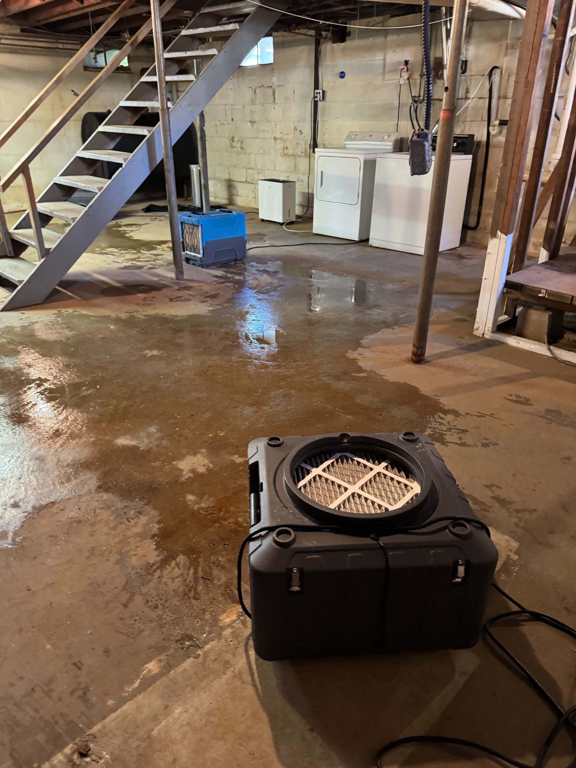 Basement with wet floor, metal stairs, and a black fan or heater in the foreground.