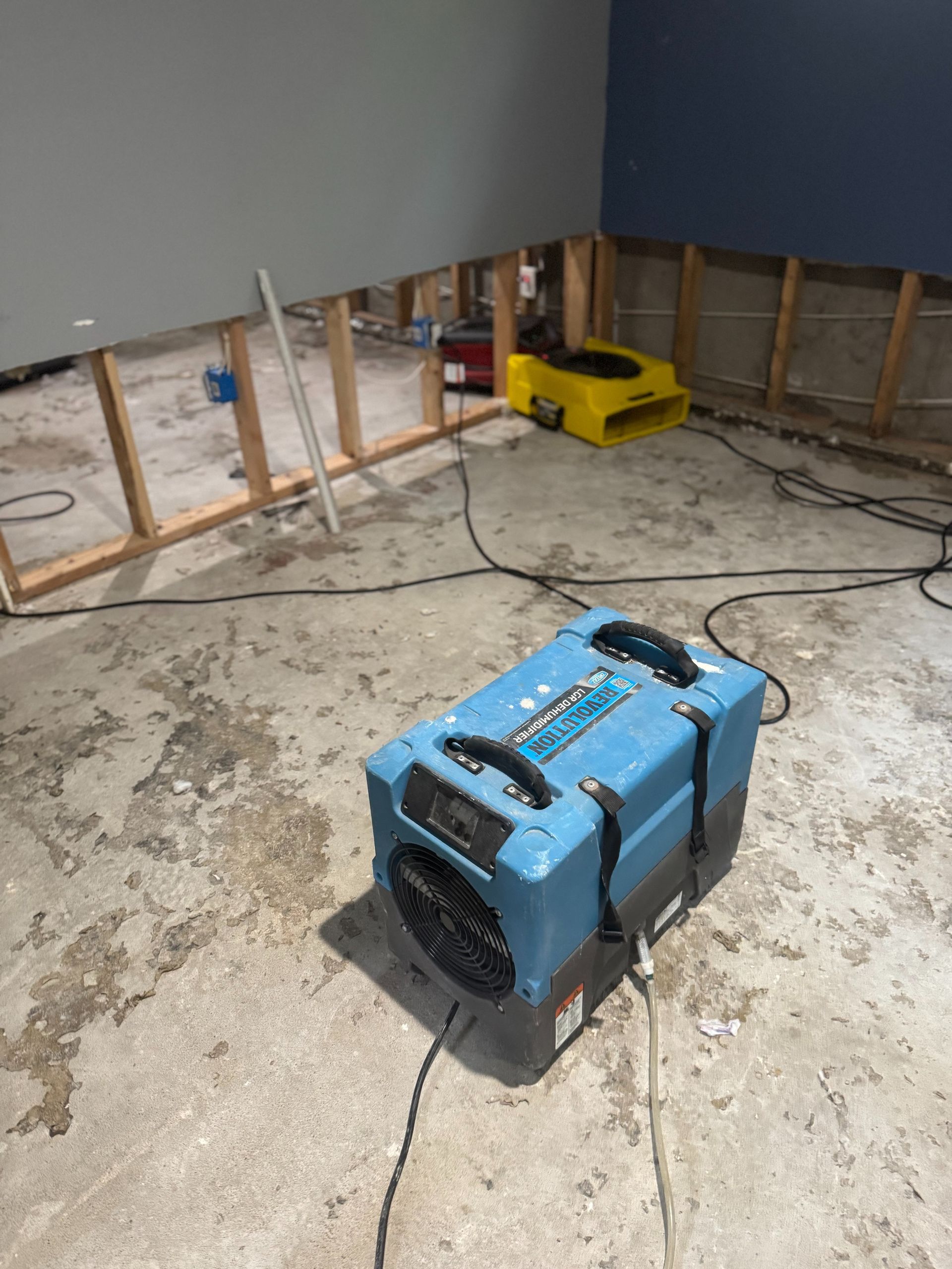 Basement with flooded concrete floor, exposed wall studs, and two portable equipment units