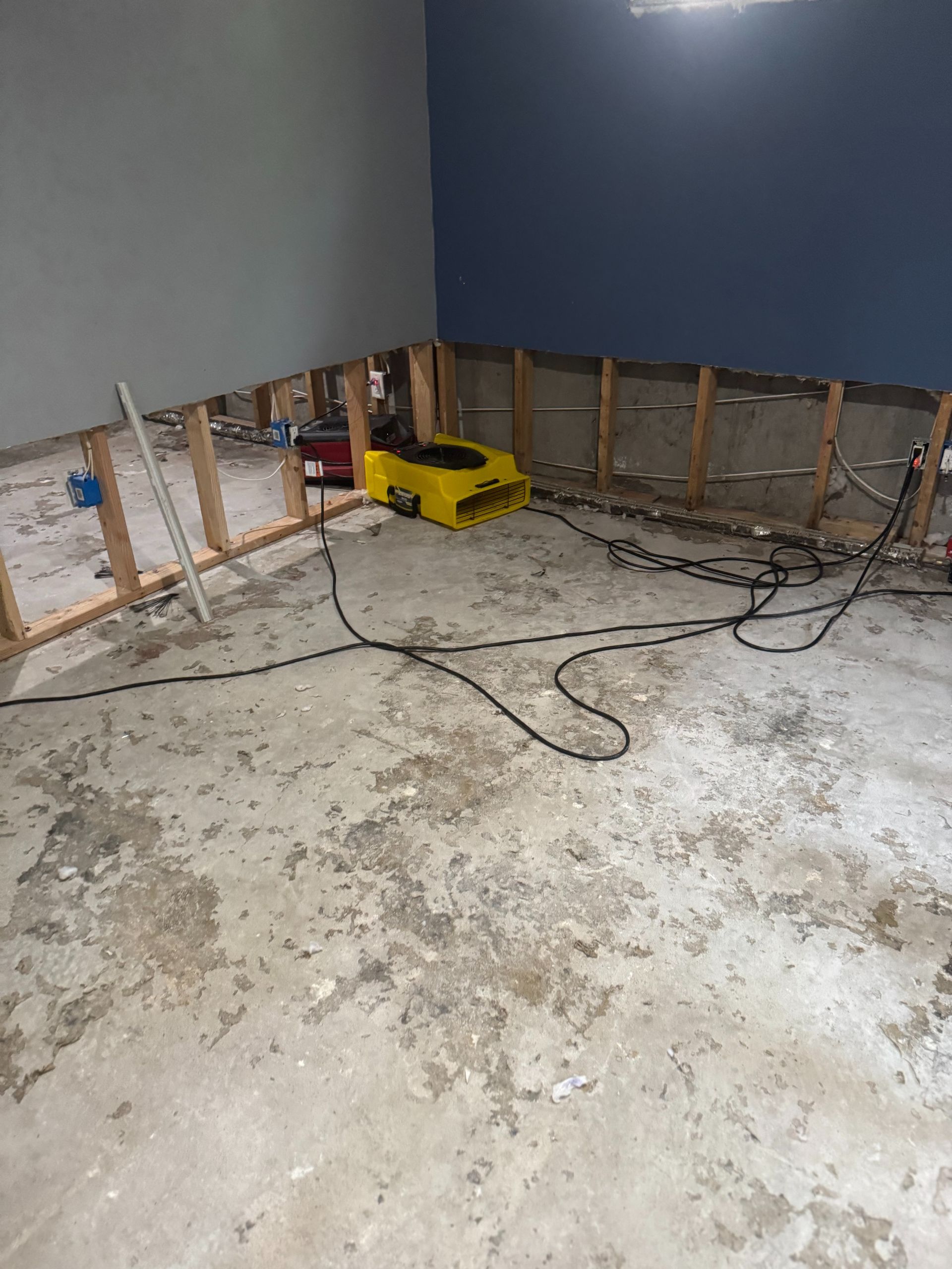 Partially demolished room with exposed wall framing, scattered cables, and a yellow toolbox on the floor
