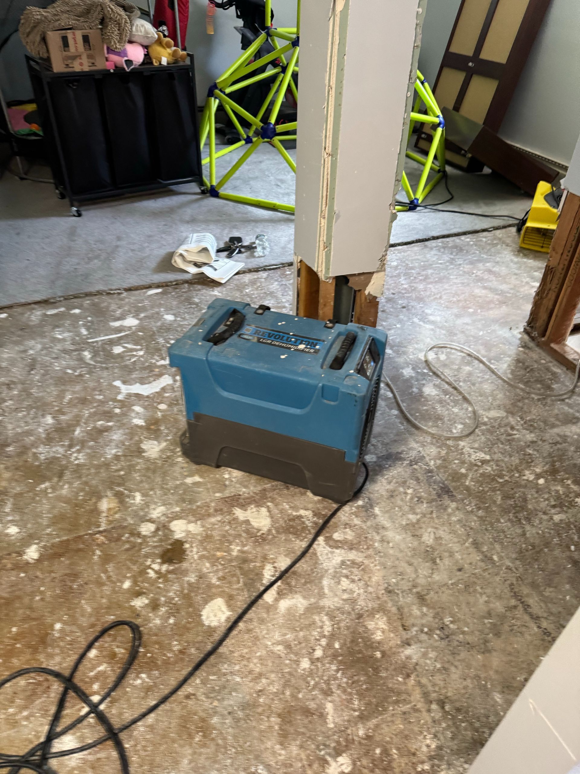 Blue dehumidifier on a wet floor near a damaged wall in a work area