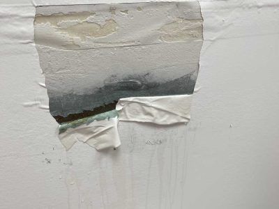 Peeling white wall paint revealing dark damaged area and torn tape at the bottom