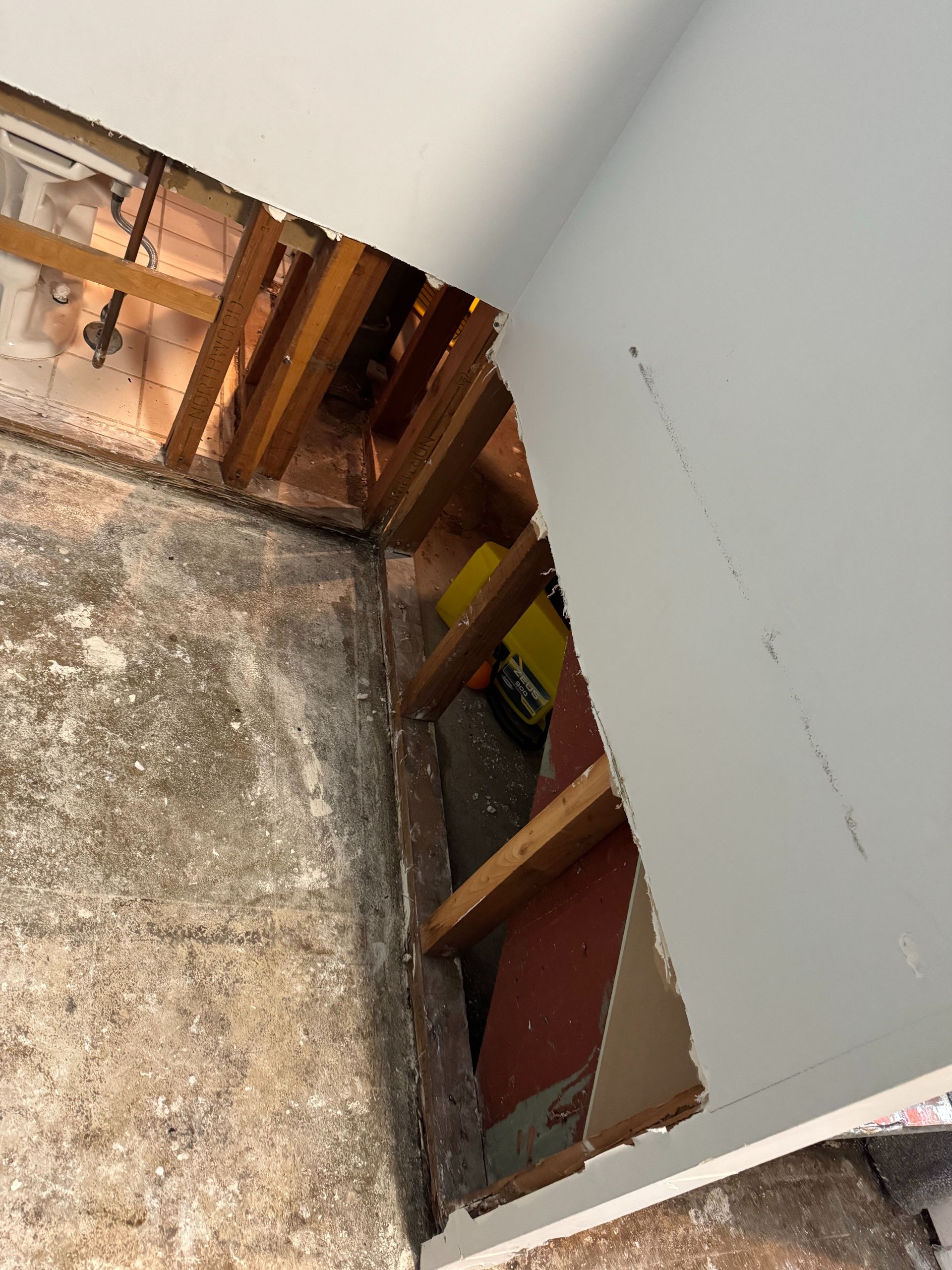 Damaged wall opening to exposed studs and insulation in a rough concrete basement area