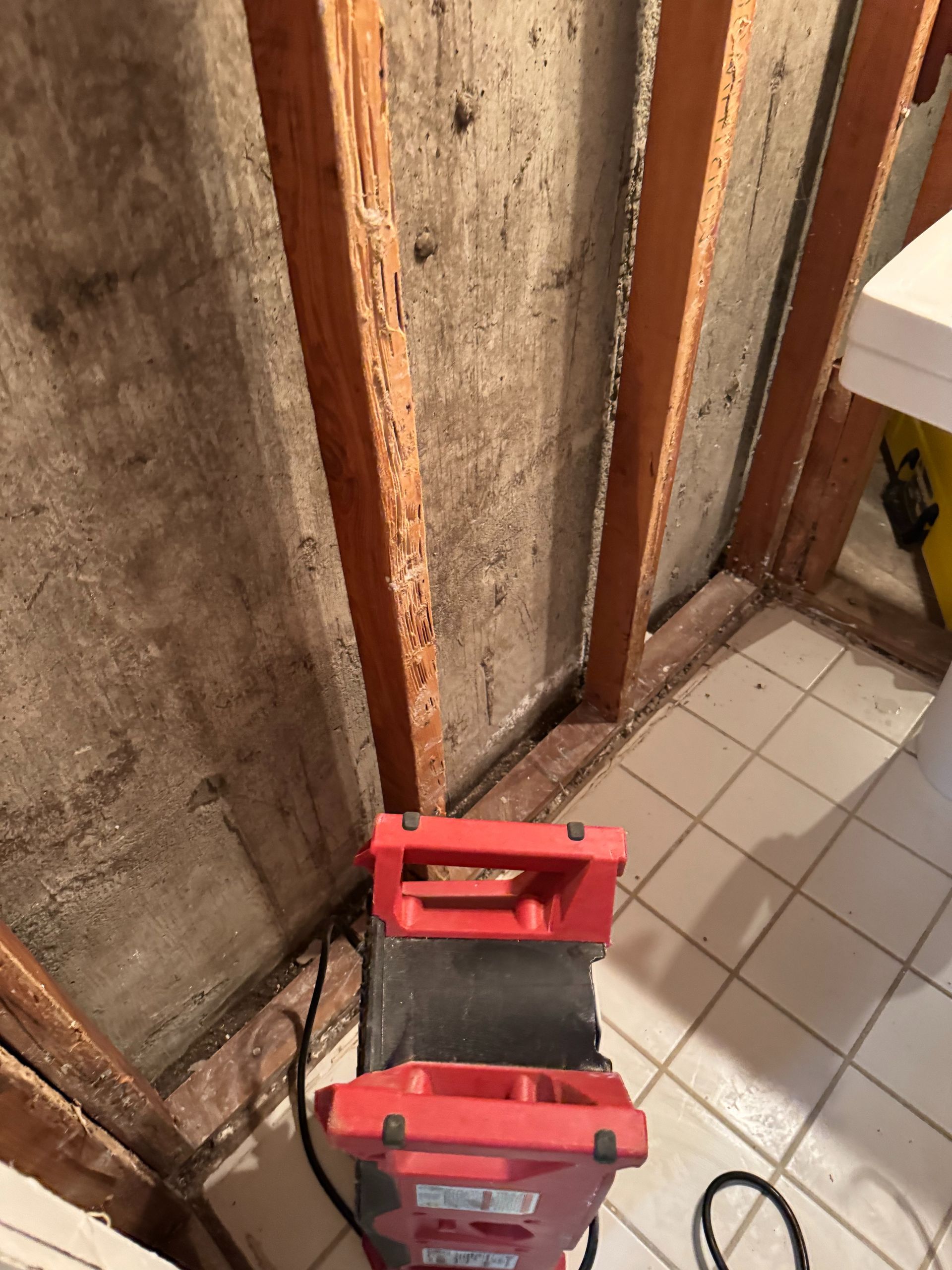 Red toolbox on a tiled floor beside exposed wall studs and old insulation in a small renovation area