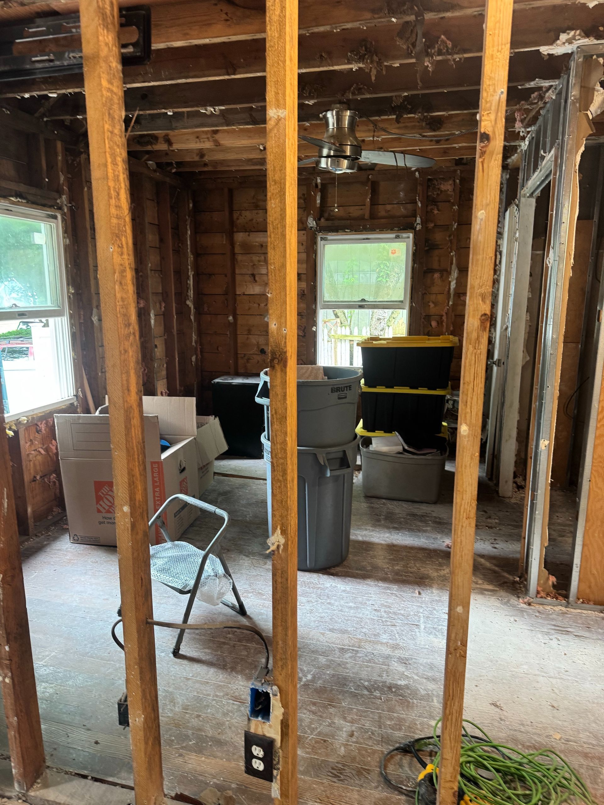 Damaged room under renovation with exposed studs, debris on the floor, and tools inside.