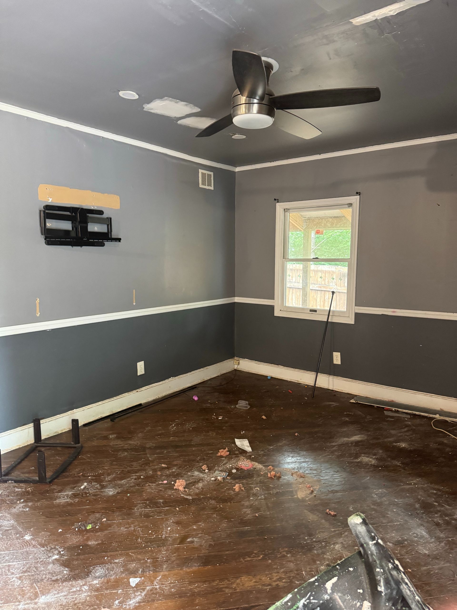Empty gray room with damaged brown floor, ceiling fan, and a window with taped paper