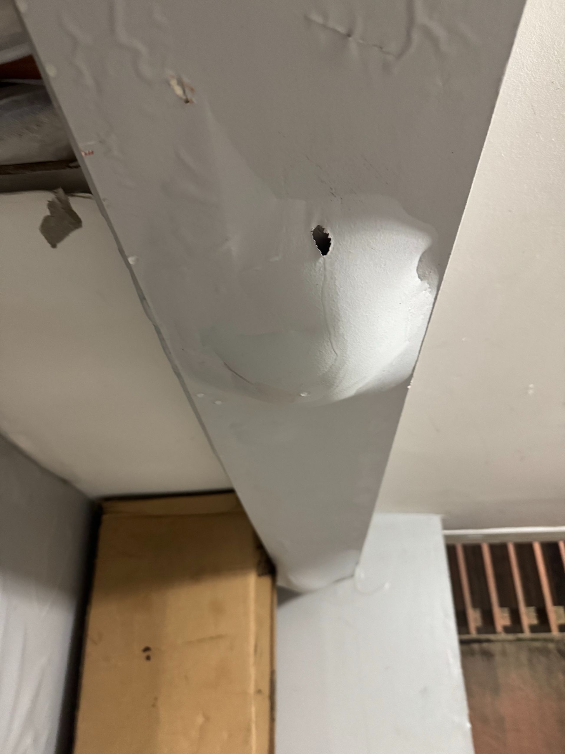 Damaged white ceiling beam with a hole and peeling paint above a wooden doorframe