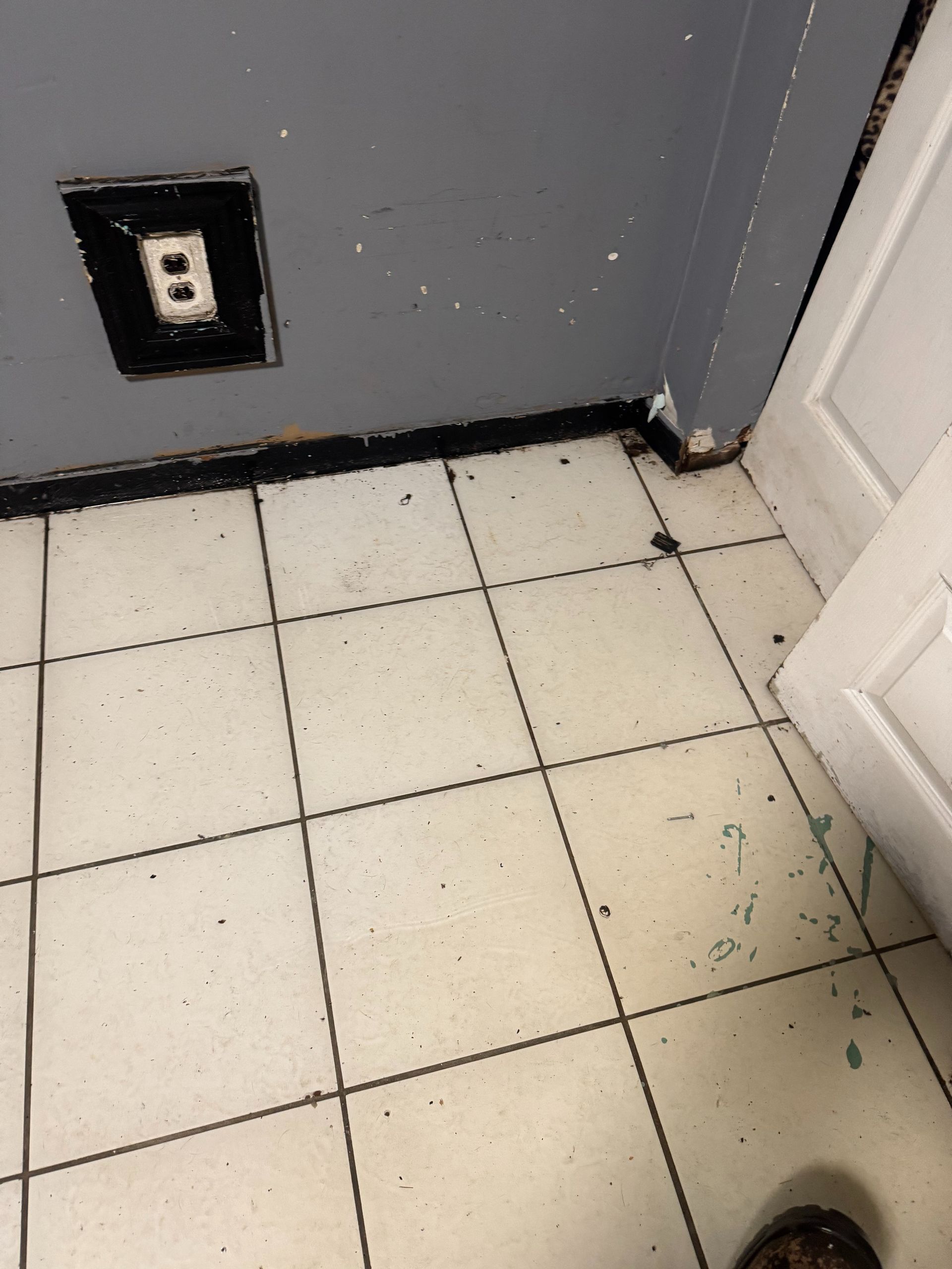 Tiled floor beside a gray wall with an electrical outlet and a white doorframe