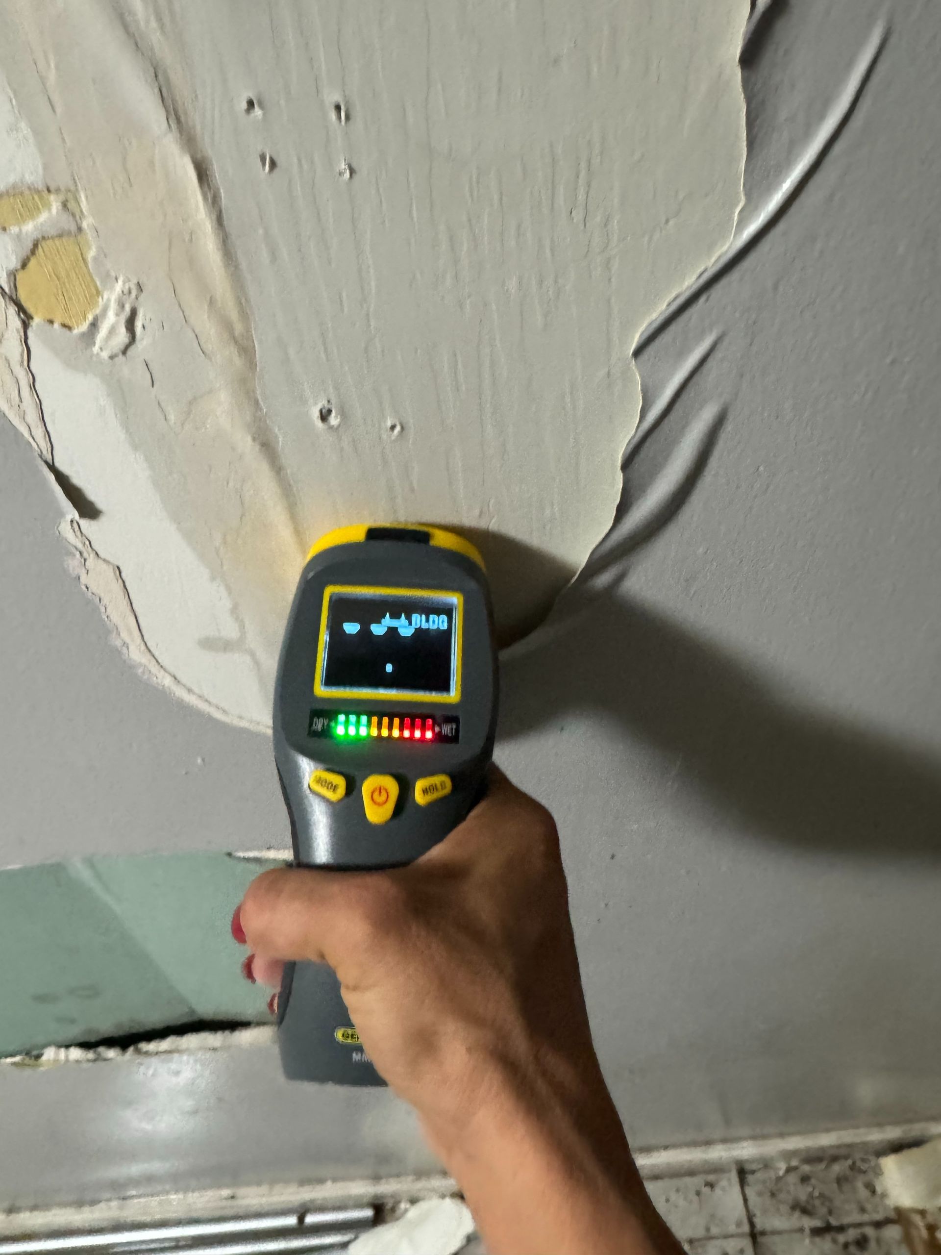 Handheld thermal camera aimed at a wall, showing heat patterns on peeling paint.