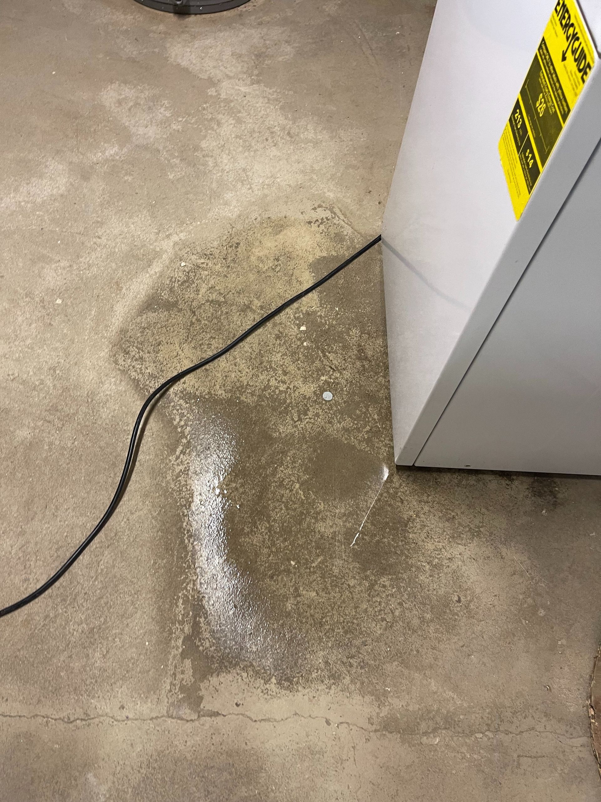 A black cord on a wet concrete floor beside a white appliance cabinet.