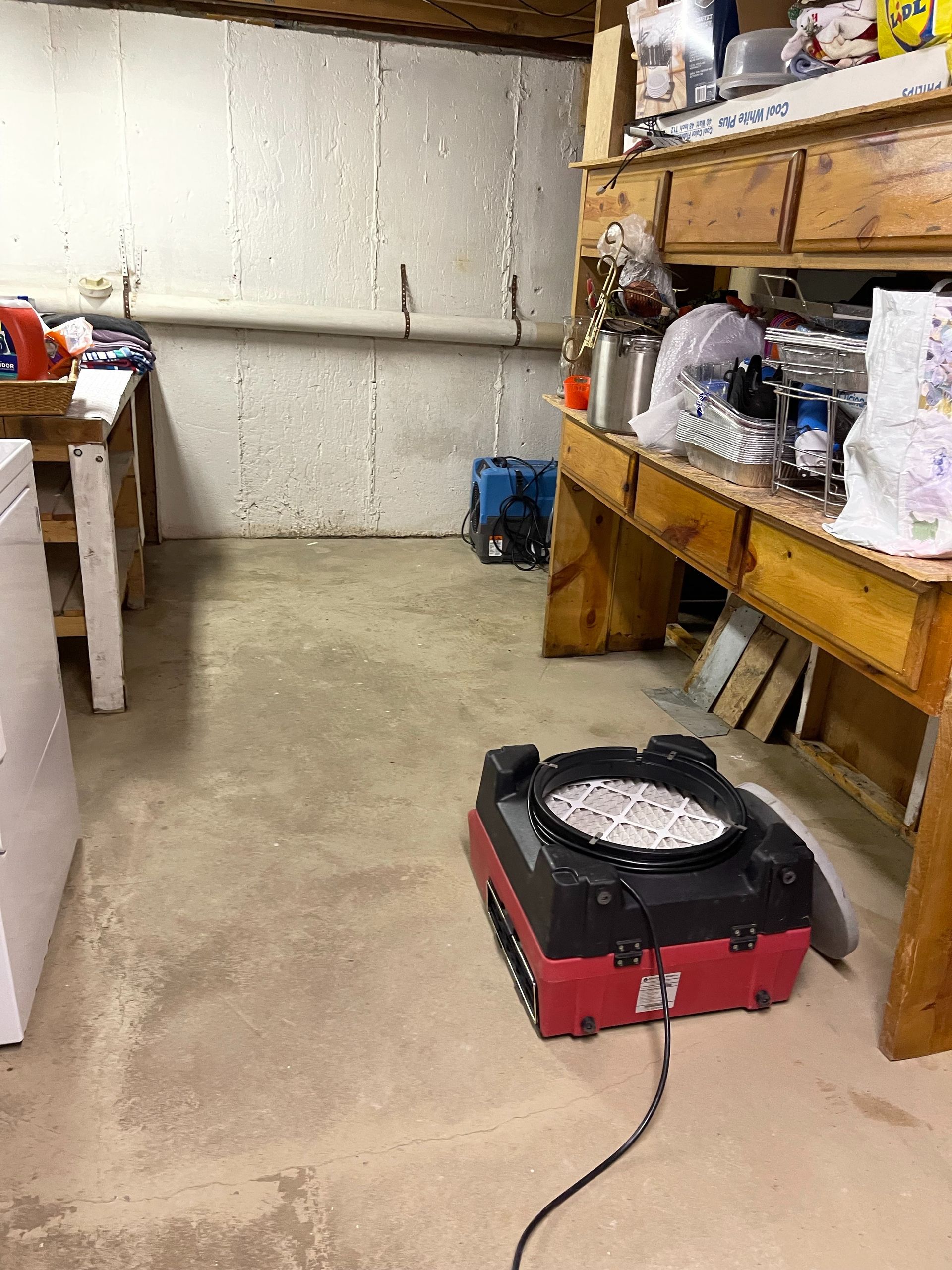 Basement workshop with a red portable fan heater on the floor near wooden shelves and a table.