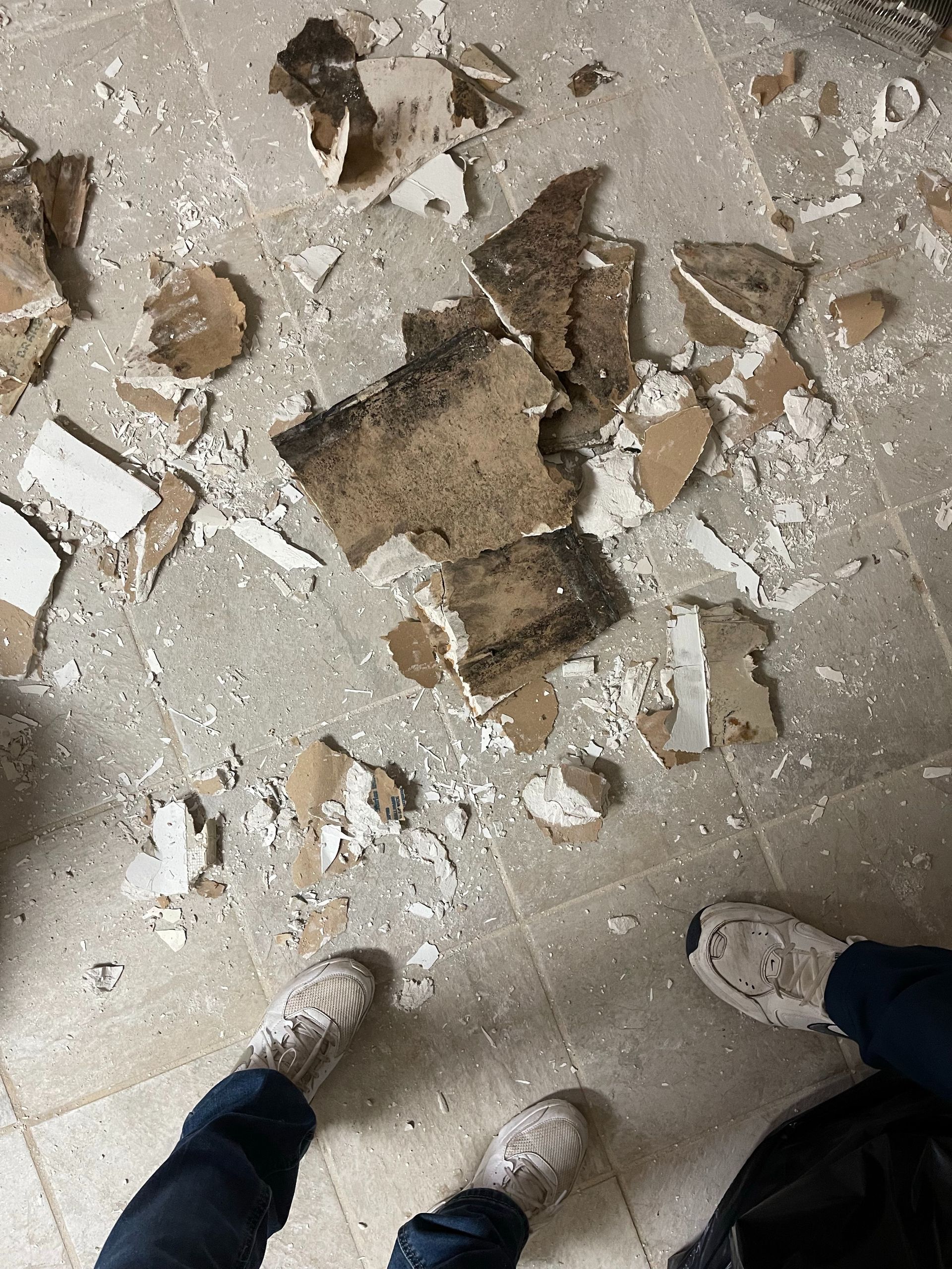 Broken cardboard and debris scattered on a dusty floor, with two shoes visible at the bottom.