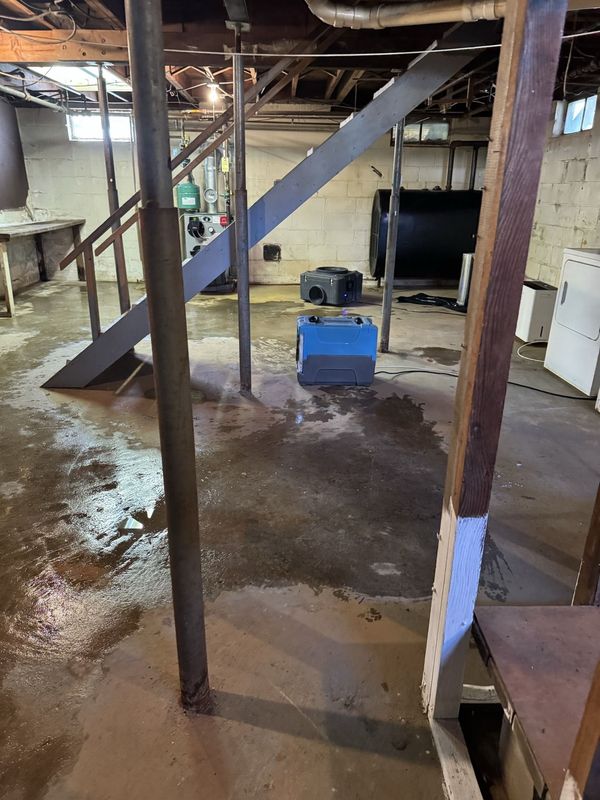 Basement with metal stairs, support posts, and a blue machine on a wet concrete floor