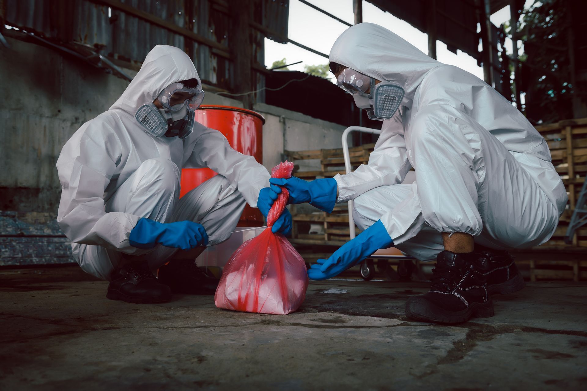 Two people in hazmat suits bagging contaminated debris in an industrial setting