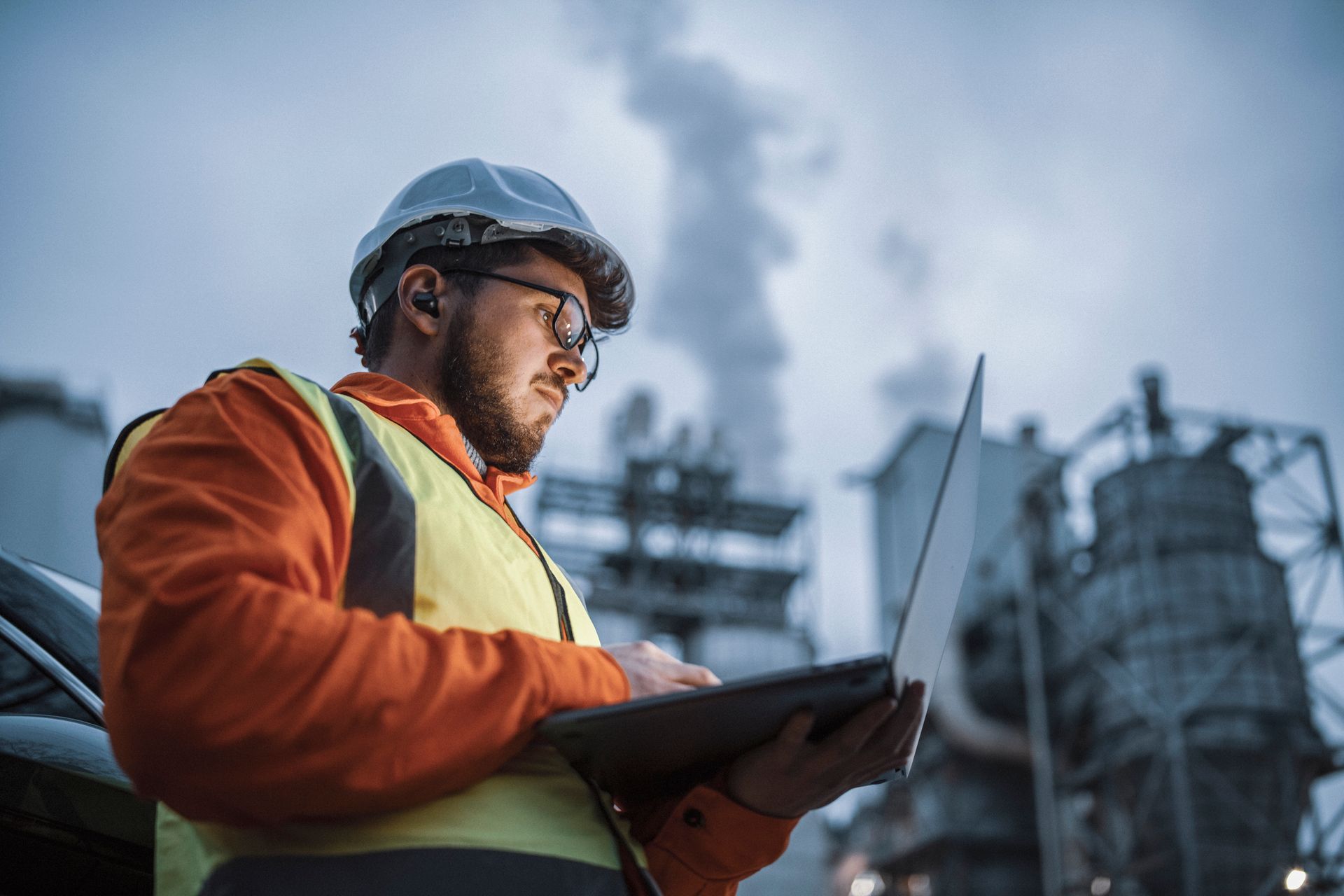 A man is using a laptop computer in front of a factory.