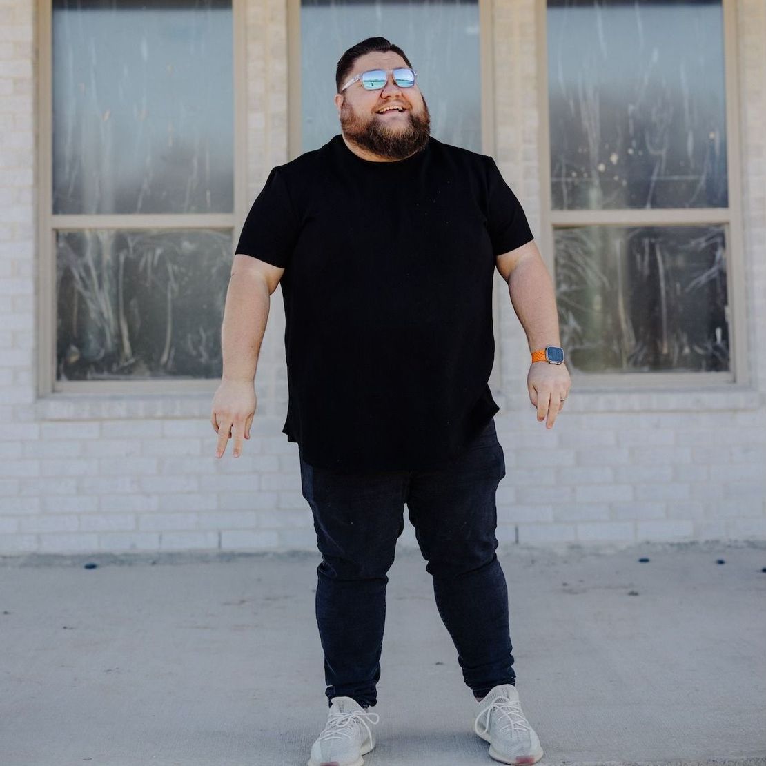 A man wearing sunglasses and a black shirt is standing in front of a building.