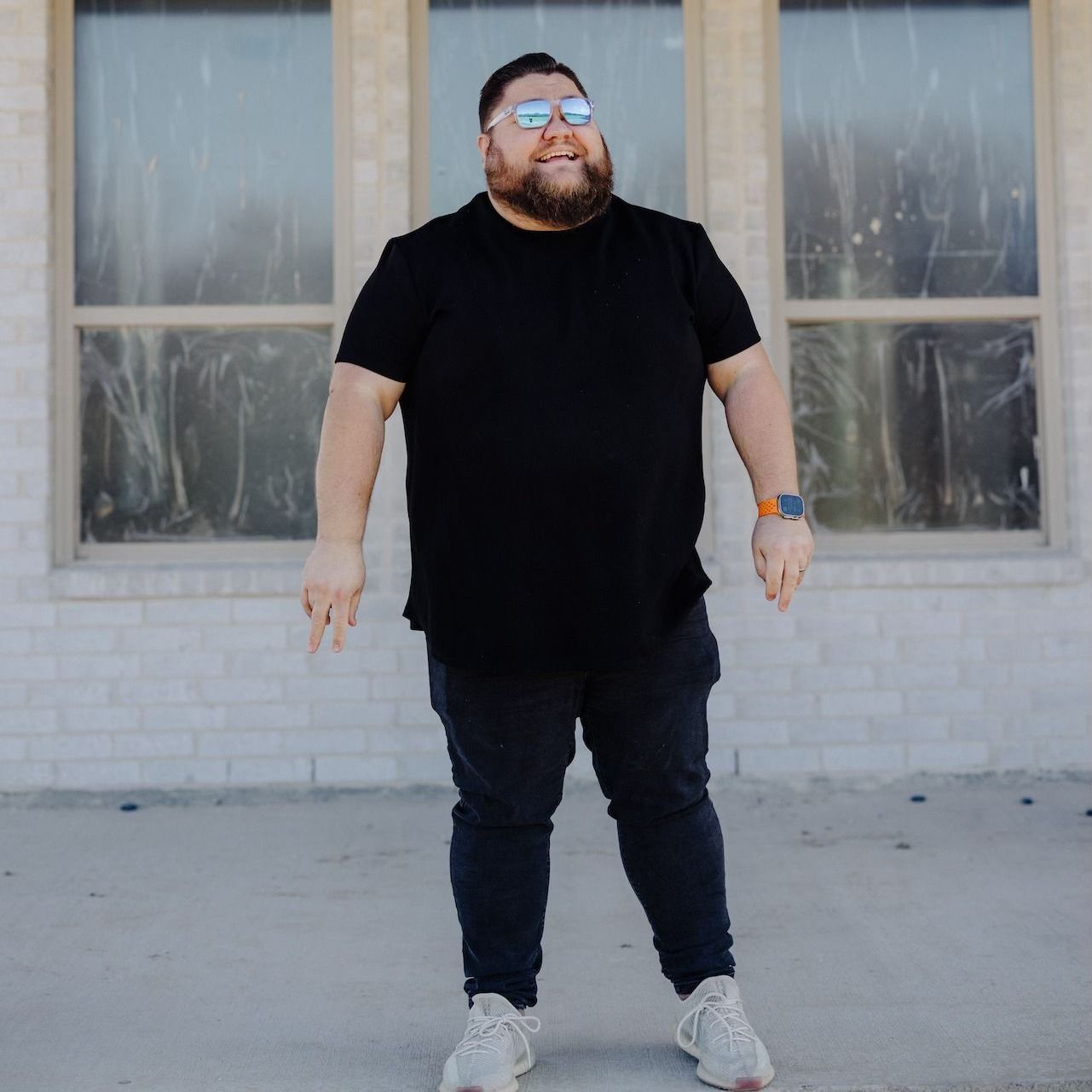 A man wearing sunglasses and a black shirt is standing in front of a building.