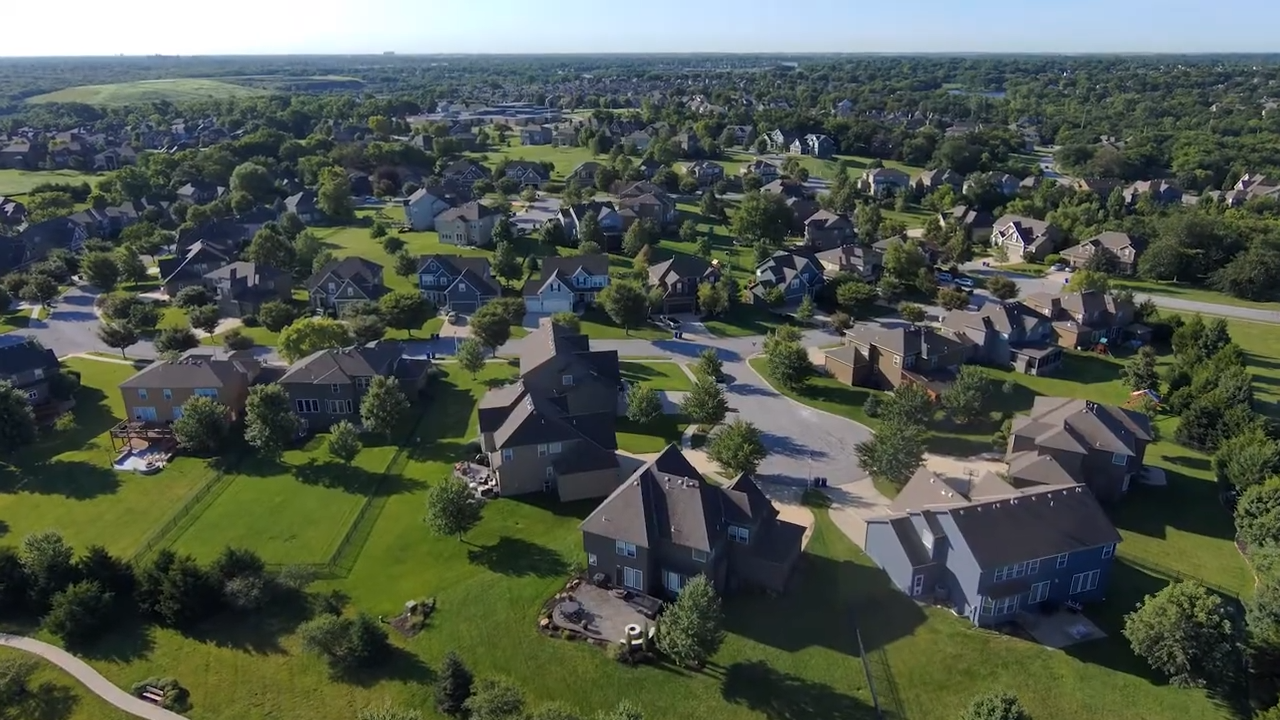Aerial view of a suburban neighborhood with houses, trees, and green lawns on a sunny day