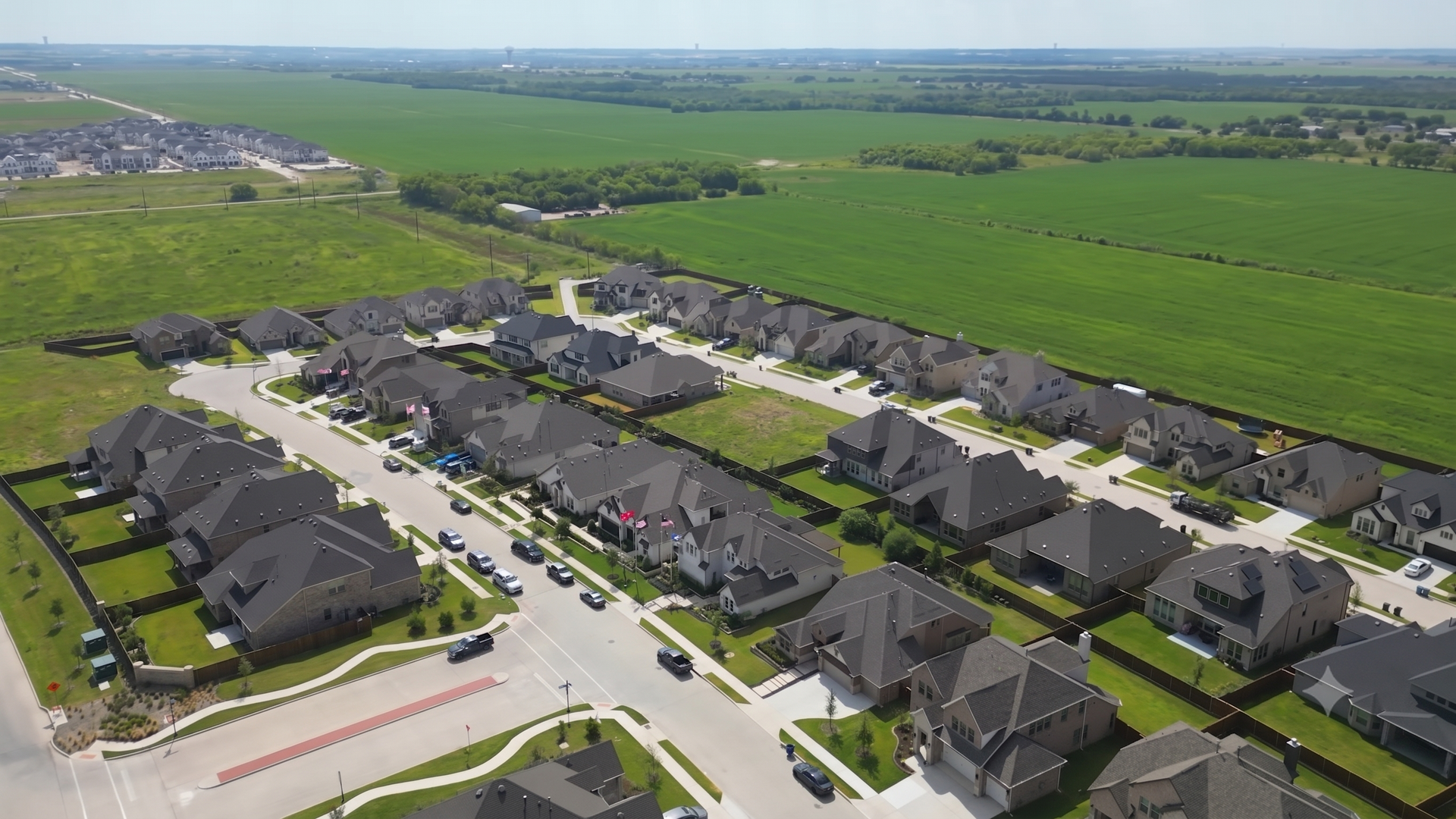 Aerial view of a suburban housing development beside open green farmland under clear skies