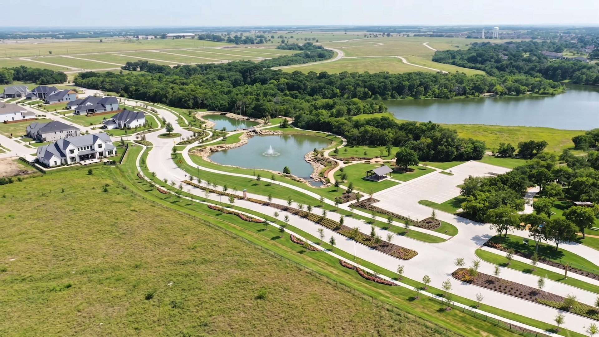 Aerial view of a suburban neighborhood with curved roads, green lawns, and a lake in the distance