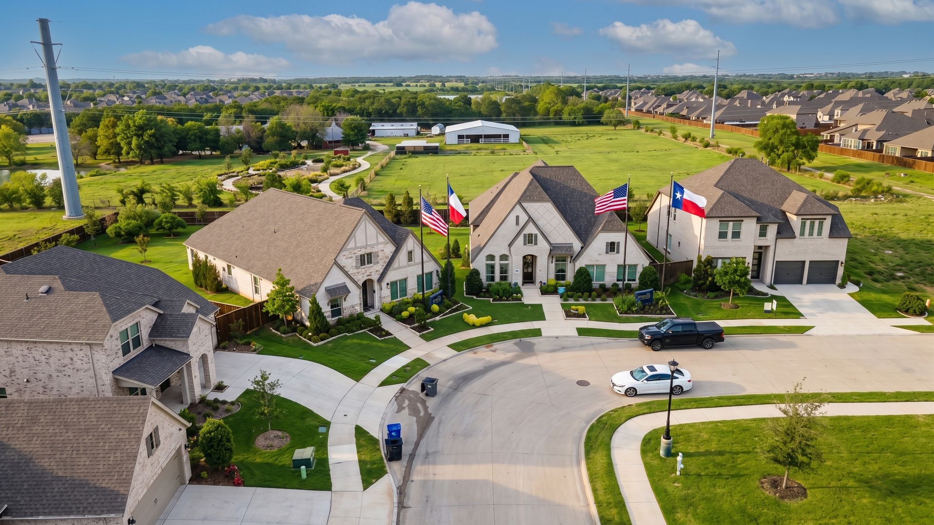 Aerial view of suburban homes with manicured lawns and parked cars on a sunny day