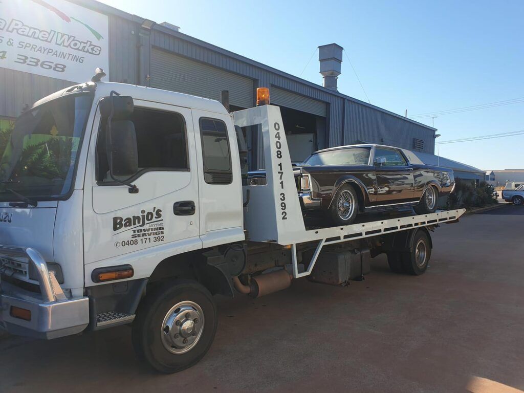 Tow truck with a black classic car on its bed, parked outside a building. — Banjo's Anytime Towing in Humpty Doo, NT