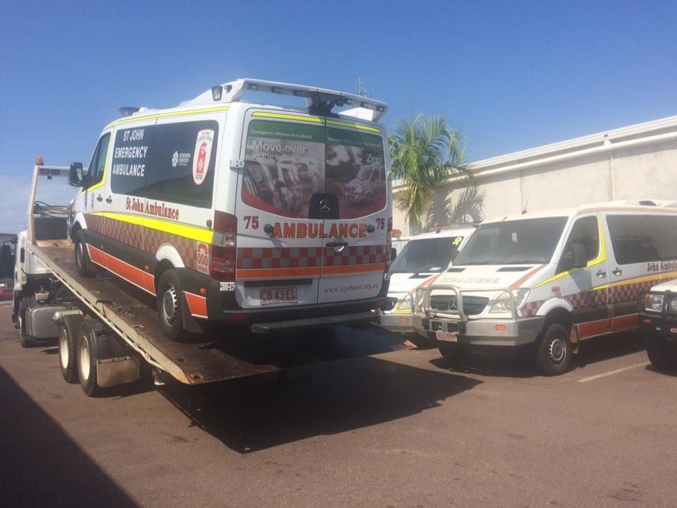 Ambulance on a flatbed tow truck next to other ambulances in a parking lot on a sunny day — Banjo's Anytime Towing in Humpty Doo, NT